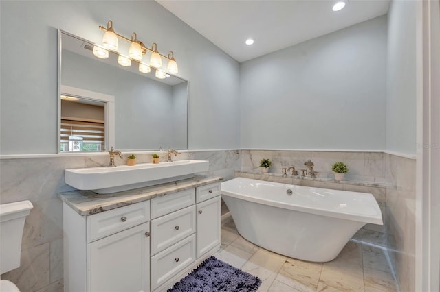 bathroom with double vanity, wainscoting, a soaking tub, marble finish floor, and a sink