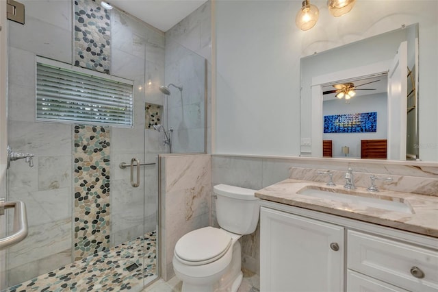 bathroom featuring toilet, a wainscoted wall, ceiling fan, a shower stall, and tile walls