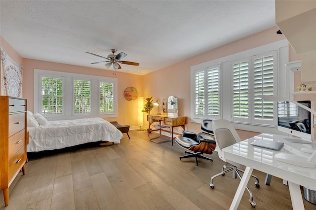 bedroom with light wood-style flooring, a ceiling fan, and a textured ceiling