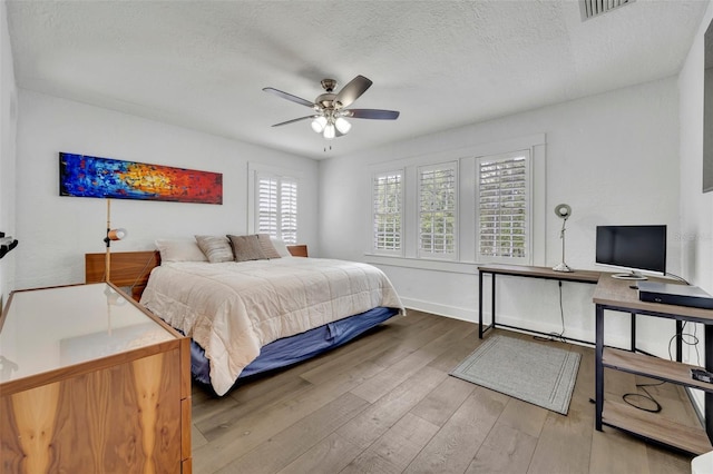 bedroom featuring baseboards, visible vents, light wood-style flooring, ceiling fan, and a textured ceiling