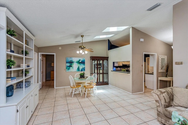 dining area with ceiling fan, light tile patterned floors, a textured ceiling, and lofted ceiling with skylight