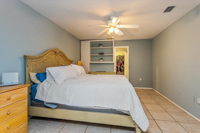 bedroom featuring a textured ceiling, light tile patterned floors, ceiling fan, and a walk in closet