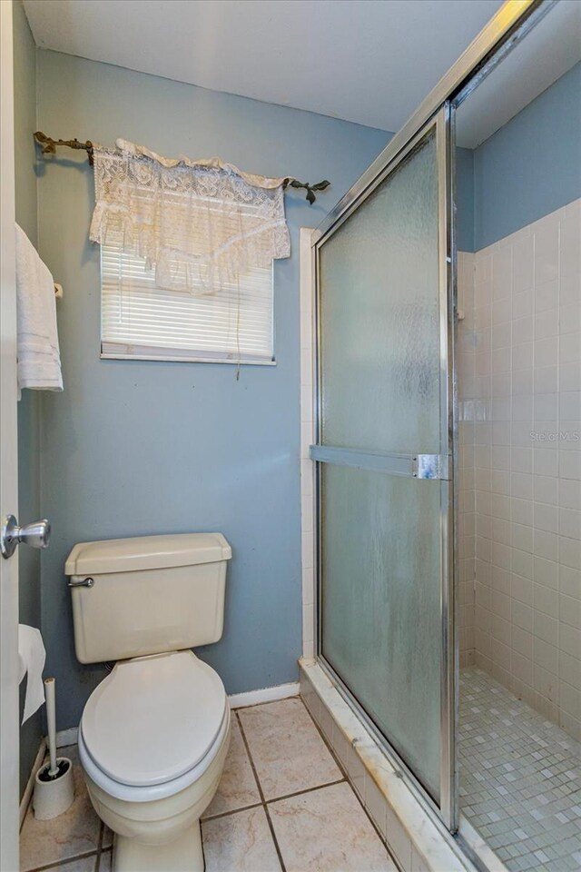 bathroom featuring tile patterned flooring, a shower with door, and toilet