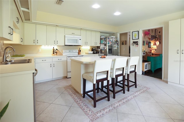 kitchen featuring a breakfast bar, a center island, sink, white appliances, and light tile patterned floors