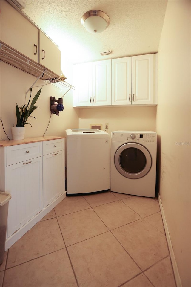 laundry area with washing machine and clothes dryer, cabinets, and light tile patterned floors