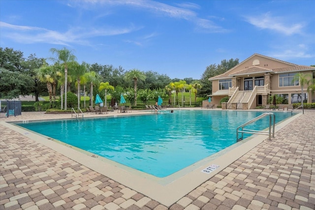 community pool with a patio area, stairs, and fence