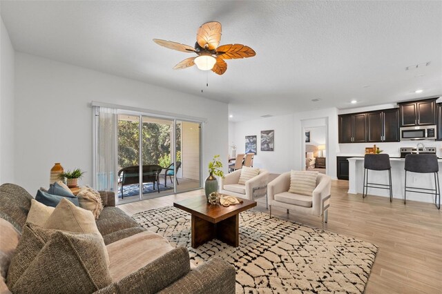 living room with ceiling fan, a textured ceiling, recessed lighting, and light wood-style floors