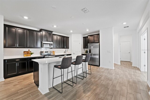 kitchen featuring light wood finished floors, visible vents, appliances with stainless steel finishes, an island with sink, and a kitchen bar