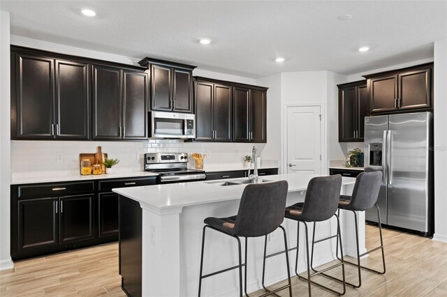 kitchen with appliances with stainless steel finishes, a breakfast bar area, a sink, and light wood-style flooring