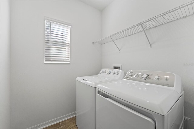 clothes washing area with laundry area, independent washer and dryer, baseboards, and wood finished floors