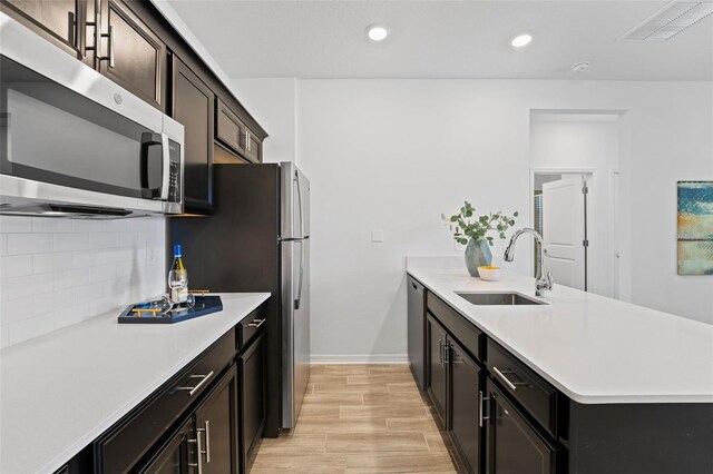 kitchen featuring stainless steel appliances, tasteful backsplash, light countertops, a sink, and a peninsula