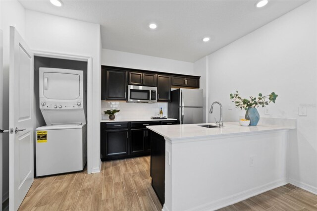 kitchen with light wood-style flooring, a peninsula, stacked washer / dryer, a sink, and appliances with stainless steel finishes