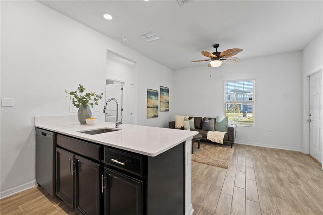 kitchen with light countertops, light wood-style flooring, stainless steel dishwasher, a sink, and a peninsula