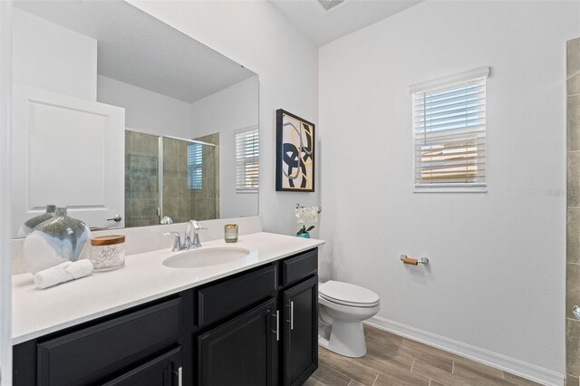 bathroom with toilet, wood finish floors, vanity, baseboards, and a stall shower