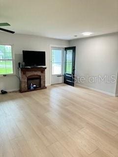 unfurnished living room featuring a fireplace with raised hearth, light wood-style flooring, and baseboards