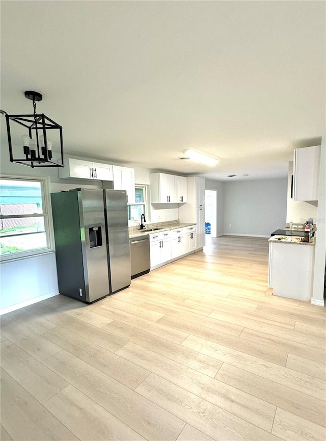 kitchen featuring appliances with stainless steel finishes, light wood-type flooring, sink, white cabinetry, and decorative light fixtures