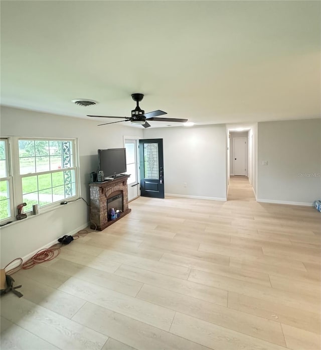 unfurnished living room with ceiling fan, light wood-type flooring, a wealth of natural light, and a brick fireplace