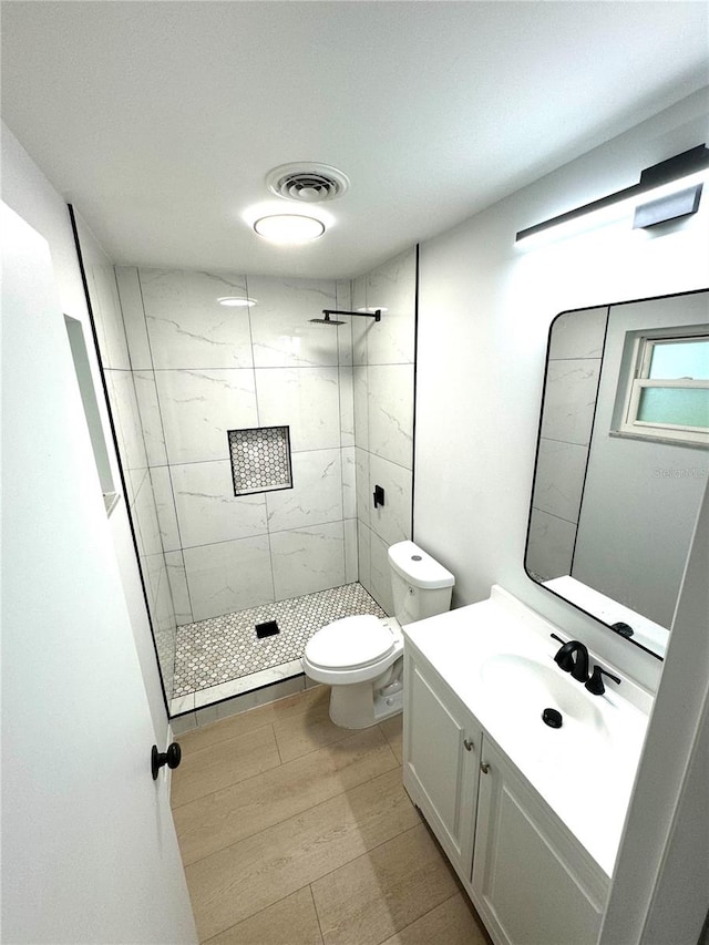 bathroom with tiled shower, vanity, tile patterned floors, and toilet