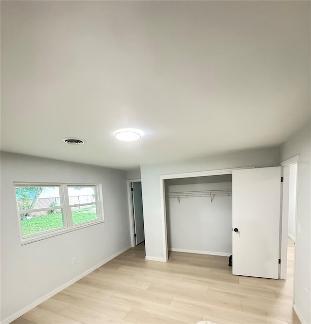 unfurnished bedroom featuring a closet, baseboards, visible vents, and light wood finished floors