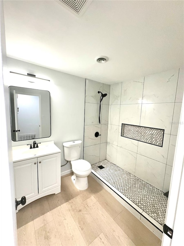 bathroom featuring vanity, a tile shower, toilet, and hardwood / wood-style floors