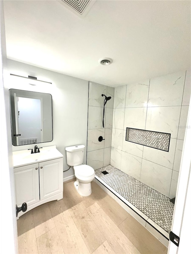 full bath featuring a tile shower, toilet, wood finished floors, and vanity