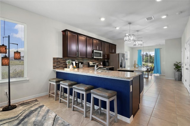 kitchen featuring light tile patterned floors, kitchen peninsula, light stone counters, stainless steel appliances, and decorative backsplash