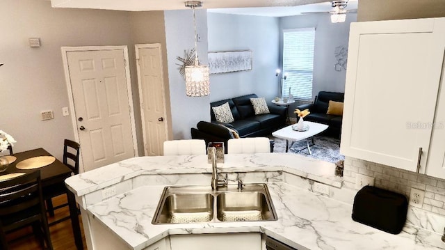 kitchen featuring pendant lighting, sink, light stone counters, white cabinets, and kitchen peninsula