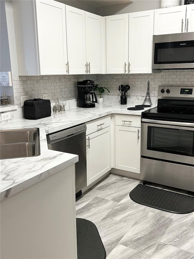 kitchen with sink, appliances with stainless steel finishes, light stone countertops, decorative backsplash, and white cabinets