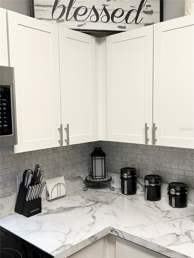 interior details featuring decorative backsplash, light stone countertops, and white cabinets