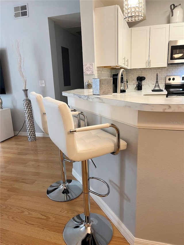 kitchen with stainless steel appliances, white cabinetry, a breakfast bar area, and decorative backsplash