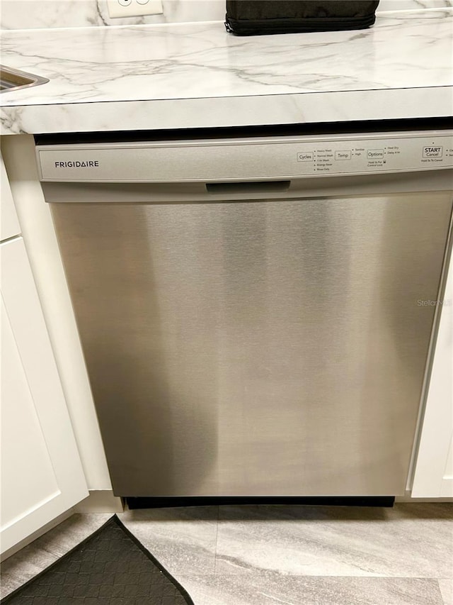 room details with white cabinets, stainless steel dishwasher, and light stone counters