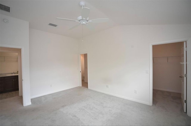 unfurnished bedroom featuring a spacious closet, light carpet, a closet, and vaulted ceiling