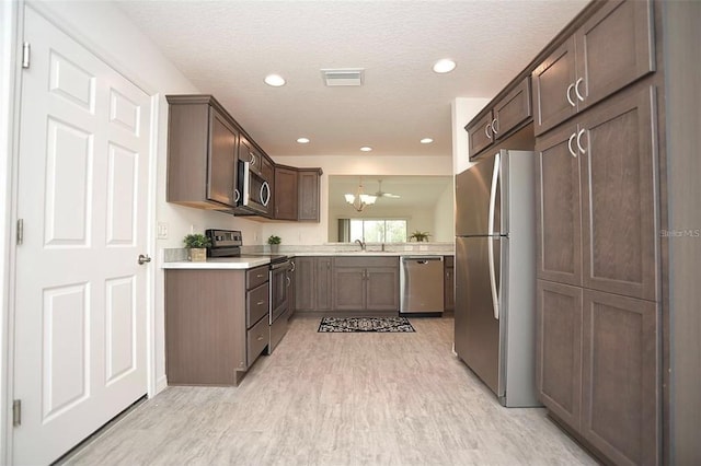 kitchen with light hardwood / wood-style flooring, stainless steel appliances, an inviting chandelier, sink, and a textured ceiling