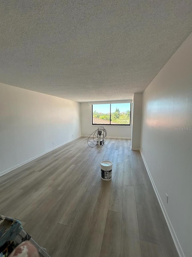 unfurnished living room featuring baseboards, a textured ceiling, and wood finished floors