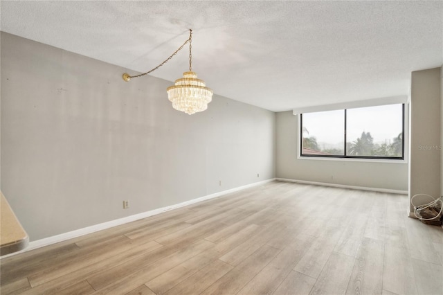 unfurnished room featuring a chandelier, a textured ceiling, and light hardwood / wood-style floors