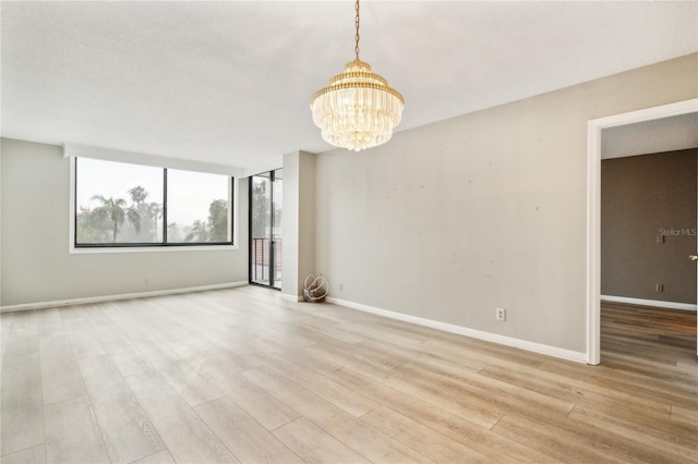 unfurnished room featuring a notable chandelier, light wood-type flooring, and a textured ceiling