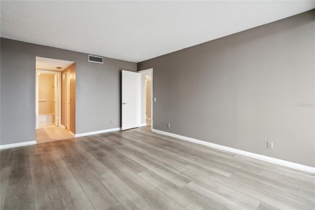 unfurnished bedroom with light wood-type flooring, a textured ceiling, and connected bathroom