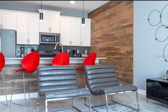 kitchen with white cabinetry, stainless steel appliances, pendant lighting, wood walls, and backsplash