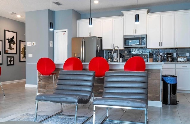 kitchen with stainless steel appliances, white cabinetry, backsplash, and decorative light fixtures