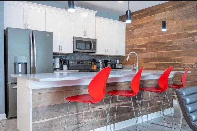 kitchen with white cabinetry, hanging light fixtures, appliances with stainless steel finishes, wooden walls, and a kitchen breakfast bar