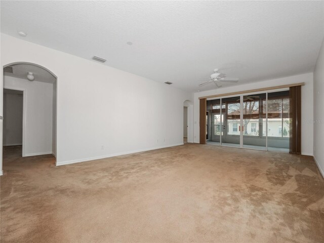 spare room featuring arched walkways, visible vents, a ceiling fan, carpet flooring, and baseboards