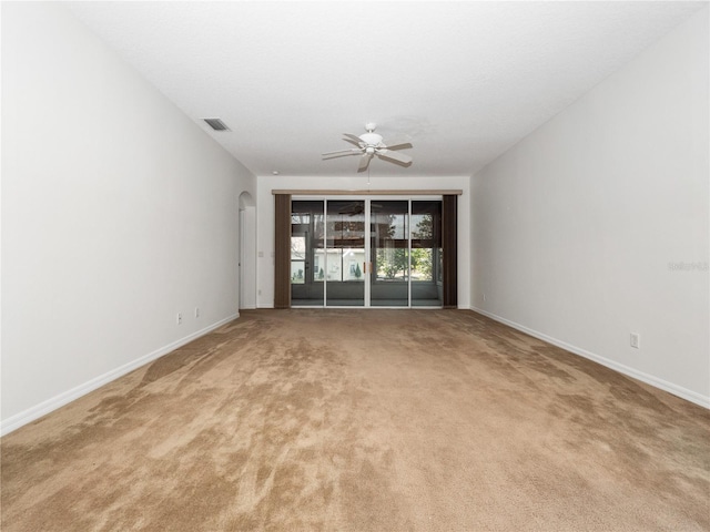 spare room featuring arched walkways, ceiling fan, light colored carpet, visible vents, and baseboards