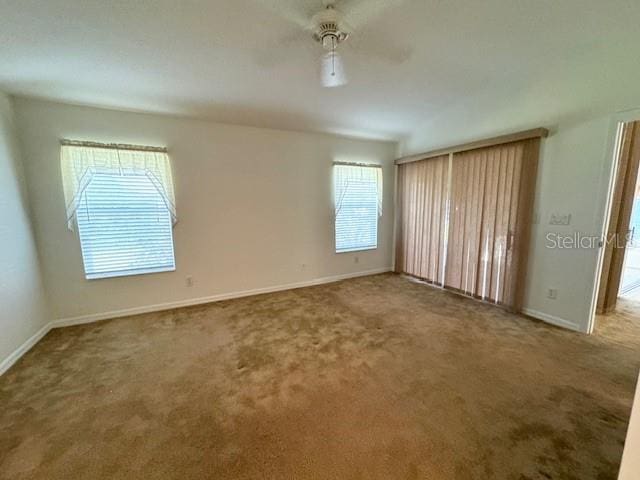 carpeted empty room with a ceiling fan and baseboards