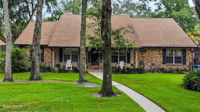 view of front of house featuring brick siding, a chimney, roof with shingles, and a front lawn