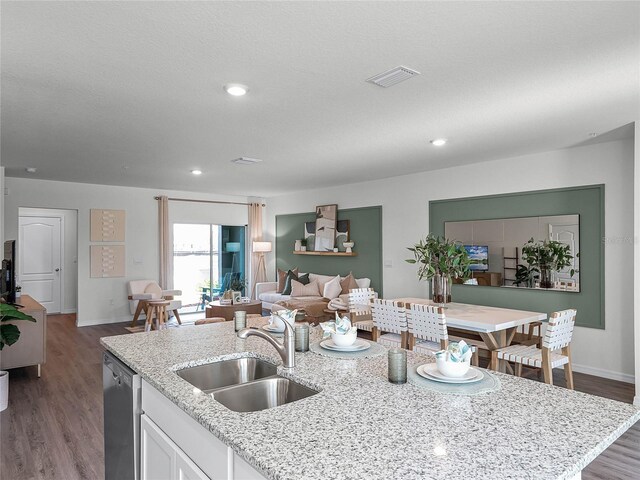 kitchen with light stone counters, an island with sink, stainless steel dishwasher, hardwood / wood-style floors, and sink