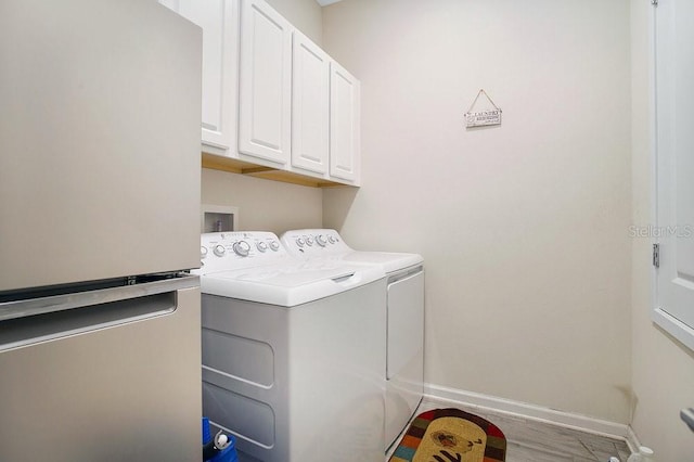 clothes washing area with washer and dryer, light hardwood / wood-style floors, and cabinets