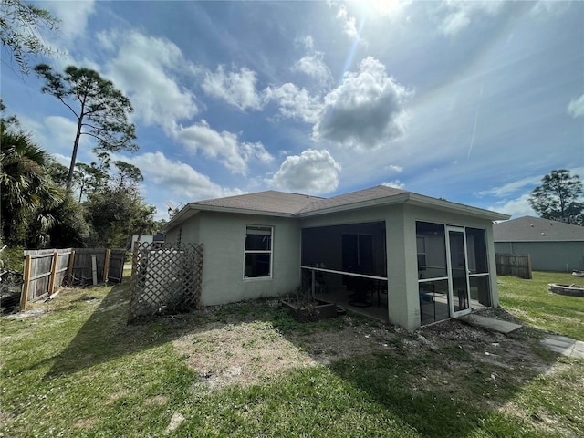 view of side of home with stucco siding, a sunroom, a yard, and fence