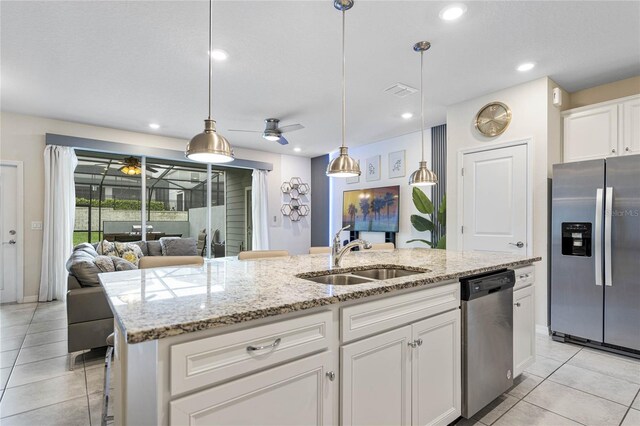 kitchen featuring sink, appliances with stainless steel finishes, light stone counters, ceiling fan, and a center island with sink