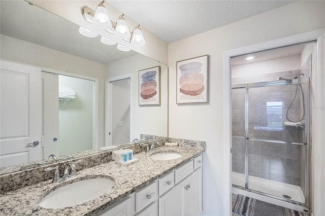 bathroom with a textured ceiling, walk in shower, and dual bowl vanity