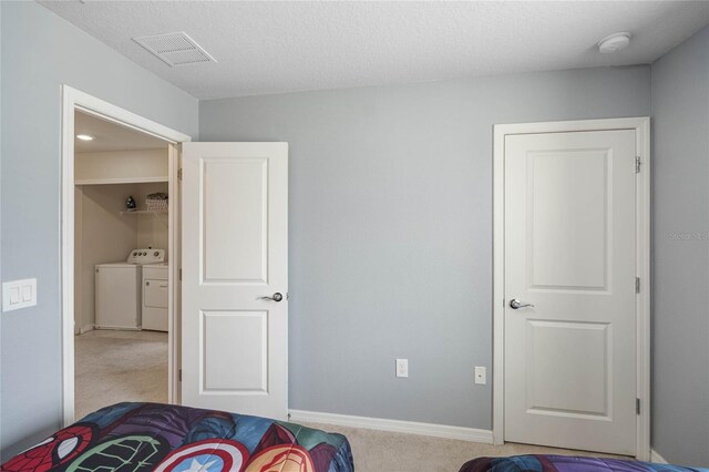 bedroom featuring a textured ceiling, washing machine and dryer, and light colored carpet